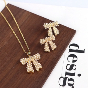Elegant gold bow jewelry set with white pearls featuring necklace and stud earrings