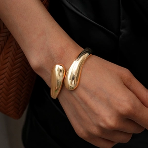 Close-up of a glossy gold geometric teardrop bracelet worn with luxury leather outfit