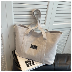 Detail of minimalist beige woven tote bag showing canvas texture and wide shoulder strap