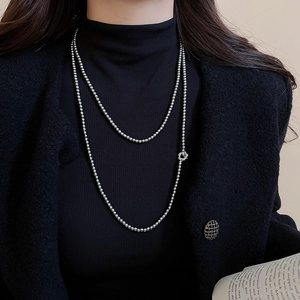 Macro detail of silver double-layered bead chain necklace featuring a floral pendant charm