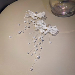 Detail of white lace bow earrings with sparkling rhinestone center and long pearl tassels