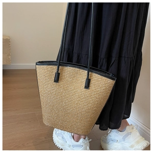 Detail view of woven straw tote bag with black faux leather trim and slender shoulder strap