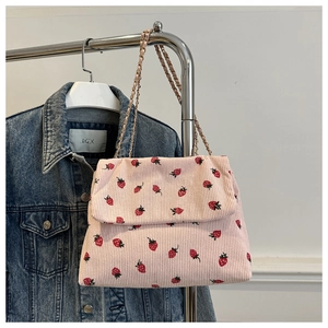 Detail of pink corduroy shoulder bag featuring embroidered strawberries and metal chain