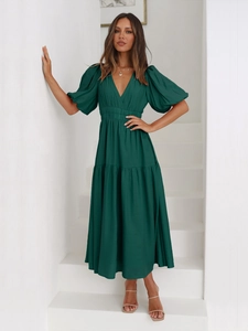 Dark green maxi dress with deep V-neck and puff sleeves shown on model in modern interior