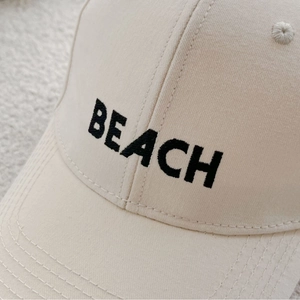 Beige cotton baseball cap with black BEACH embroidery in a clean close-up view