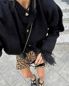 Details des schwarzen Strick-Cardigans mit goldenen Herzknöpfen und Federbesatz