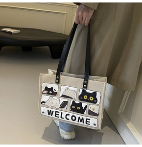 Close-up of beige cat canvas tote bag with black leather straps and golden rivets