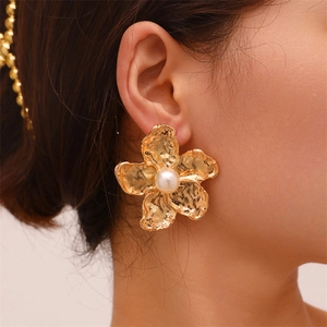 Close-up of golden leaf-shaped earrings with central pearl on a real-life model