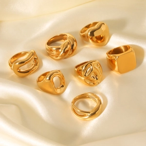 Macro shot of 7 gold geometric rings set on cream silk fabric showing heart and cutout patterns