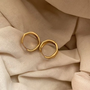 Minimalist gold brushed geometric hoop earrings on textured beige fabric background