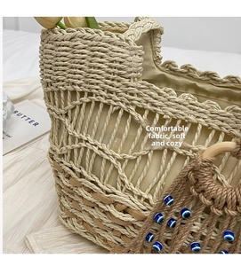 Detail of woven straw tote bag with wavy edges and blue eye tassel accessory on white fabric