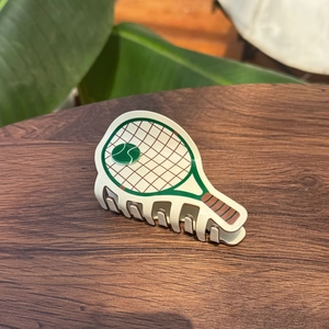 Détail d'une pince à cheveux raquette de tennis en acétate sur une table en bois sombre