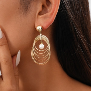 Detail of layered gold geometric earrings with pearl pendant worn by a model
