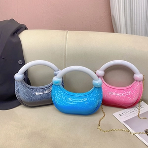 Three acrylic half-moon evening bags with glitter finish and round handles on a sofa