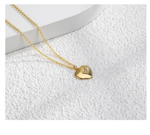 Close-up of golden heart pendant with wing texture on a minimalist fine chain