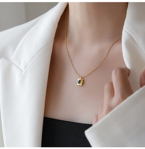 Detail of a square green crystal pendant on a gold chain necklace worn by a model