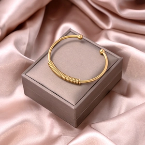 Detailed view of a gold spiral open cuff bracelet on a soft pink satin fabric
