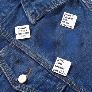 Set of seven minimalist white enamel square brooches with black inspirational quotes on denim