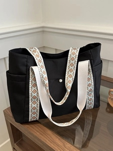 Borsa tote in tela nera con tracolle geometriche e tasche laterali su una scrivania