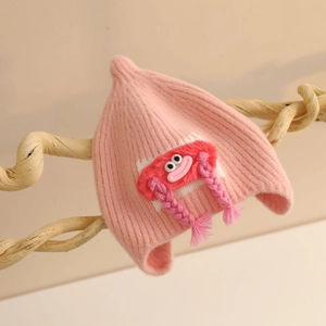 Close-up of pink knitted baby hat featuring cute red cartoon monster and braided tassels