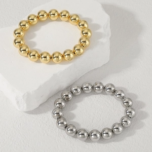 Dettaglio dei bracciali con perline in oro e argento lucido su sfondo in pietra bianca