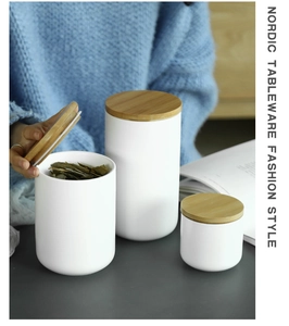 Three white ceramic storage jars with wooden lids and tea leaves in a Nordic kitchen setting