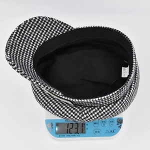 Detailed view of black and white houndstooth baker boy cap on a scale showing 123g weight