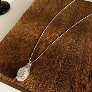 Macro shot of a silver braided bottle pendant on a ball chain over a wooden surface
