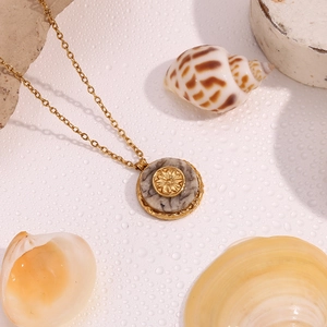 Detail of 18K gold necklace with marble sun pendant displayed among sea shells