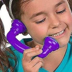 Smiling girl playing with a purple plastic toy telephone receiver on white background