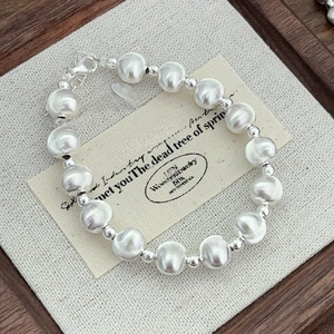 Detailed top view of silver bead bracelet with lobster clasp on a wooden jewelry tray