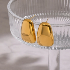 Polished gold teardrop earrings hanging on textured glass with a marble background
