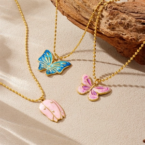 Gold-plated necklaces with blue butterfly and pink tulip enamel charms on wood background