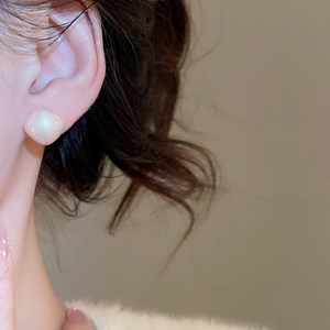 Detail of square geometric stud earrings in pearlescent cream on a model ear