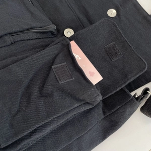 Detail of black canvas multi-pocket messenger bag showing stitching and metal fasteners