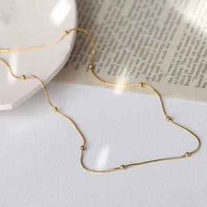Minimalist gold beaded snake chain necklace displayed on a textured white surface