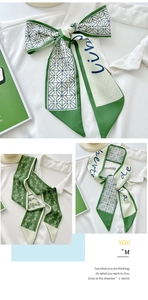 Close-up of green silk scarf with floral pattern and script text tied on white shirt