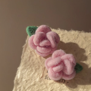 Close-up of pink flocked rose earrings with green leaves on a textured paper background