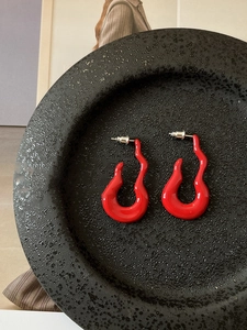 Detail of red hollow wave curved earrings placed in a black textured display bowl