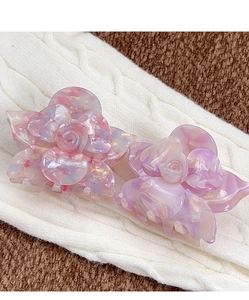 Close-up of pink and purple acetate flower hair claws on a soft white knit fabric