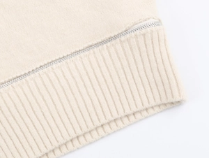 Détail du pull en maille beige montrant la texture côtelée et la fermeture éclair argentée