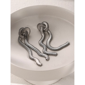 Macro shot of silver knot earrings with snake chain texture in a white ceramic bowl