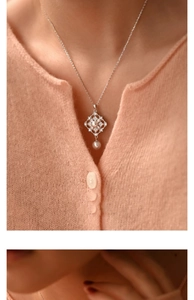 Detail of silver pearl necklace with zircon flower pendant on a beige knit sweater