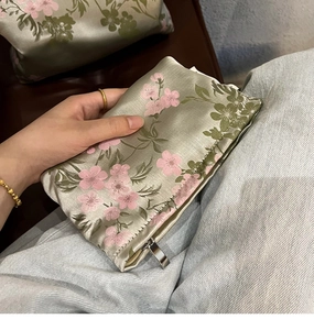 Detail of light green satin cosmetic bag with pink flower patterns and metal zipper