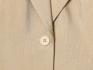 Detail van de champagne goudkleurige blazerstof met metaalglans en bijpassende knopen