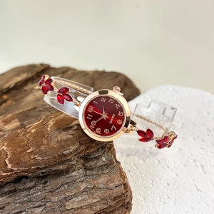 Elegant gold quartz watch with red leaf gems and matching dial on a luxury stand