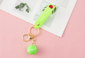 Close-up of neon green tennis ball keychain with Good Luck wrist strap and gold metal clasp
