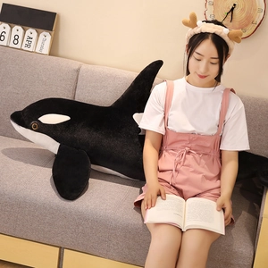 Large killer whale plush pillow on sofa next to woman reading in a cozy living room