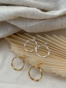 Detail of twisted round hoop earrings in gold and silver on a rustic palm leaf backdrop