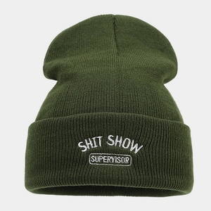 Dettaglio del ricamo bianco SHIT SHOW SUPERVISOR su un berretto in maglia verde scuro